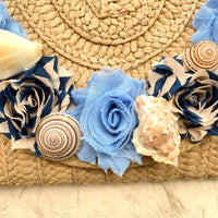 Seashells, navy striped fabric rosette, and light blue fabric rosette on a straw clutch purse for women.