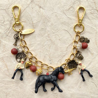 Western bag charm for handbags. Bag chain for handbag with two clasps, two cowboy charms, red beads, bronze charm including a mini bucket, owl, fan, tree and flower with a black horse figurine hanging in the middle. Lenora Dame bag charms.