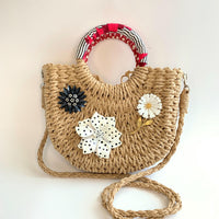Cute straw bag for summer detailed with large metal flower brooches and contrast top handle wrapped in red and black fabric. Small woven handbag for casual summer style.