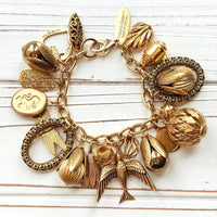 Chunky gold charm bracelet filled with a mix of gold charms in different shapes and sizes hung on a gold cable chain with lobster clasp. Lenora Dame jewelry made in the USA.