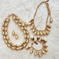 Two strand gold necklace with cream pearls encased in gold leaf bead caps, pearl and gold earrings, a gold necklace with dangling pearls with gold leaf bead caps, and a gold charm bracelet with cream pearls in gold leaf bead caps. Lenora Dame jewelry.
