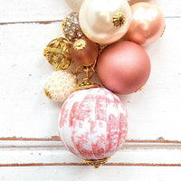 Beaded bag charm with a mix of bead styles in shades of pink, peach, gold and pearl. One larger round bead in a pink and white toile print hangs at the bottom and a gold trigger clasp on top of all of the beads. Brass oval hang tag near the trigger clasp that says "Lenora Dame Handmade in USA". Lenora Dame bag charm.