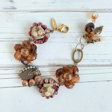 A brown and gold beaded bracelet with a heart-shaped charm, a flower charm, and a leaf charm. The bracelet has a gold clasp and a tag that reads &#39;amore di amore&#39;. Upcycled vintage earring bracelet for women with brown tone repurposed earrings crafted into a link bracelet with antique bronze finish. Lenora Dame bracelet handmade in the USA.