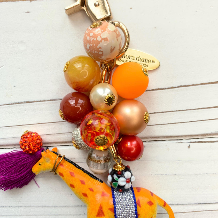 Cute beaded bag charm with embellished giraffe figurine and a mix of beads in orange and red tones.