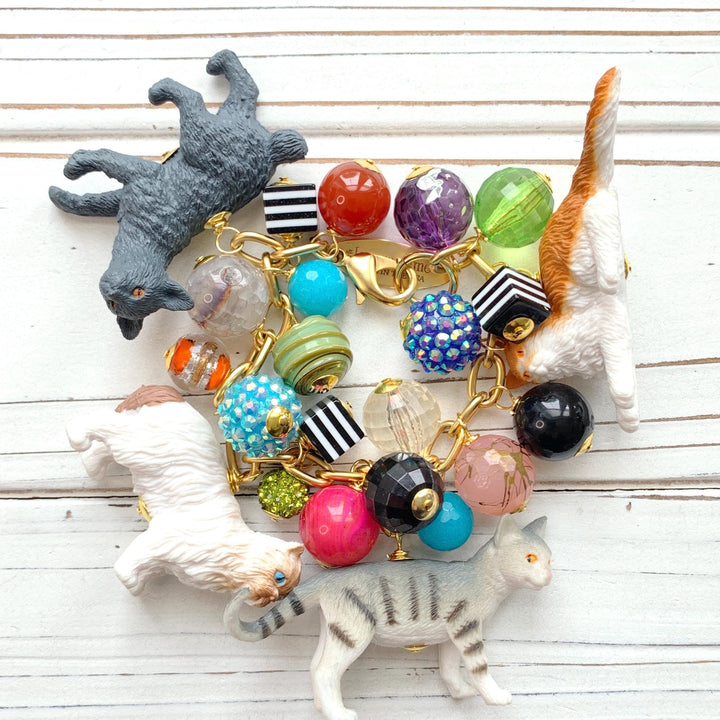 A charm bracelet with colorful beads, including red, green, blue, yellow, and purple. The bracelet also features small cat figurines in white, black, and gray. Gift for cat lovers. Lenora Dame jewelry.