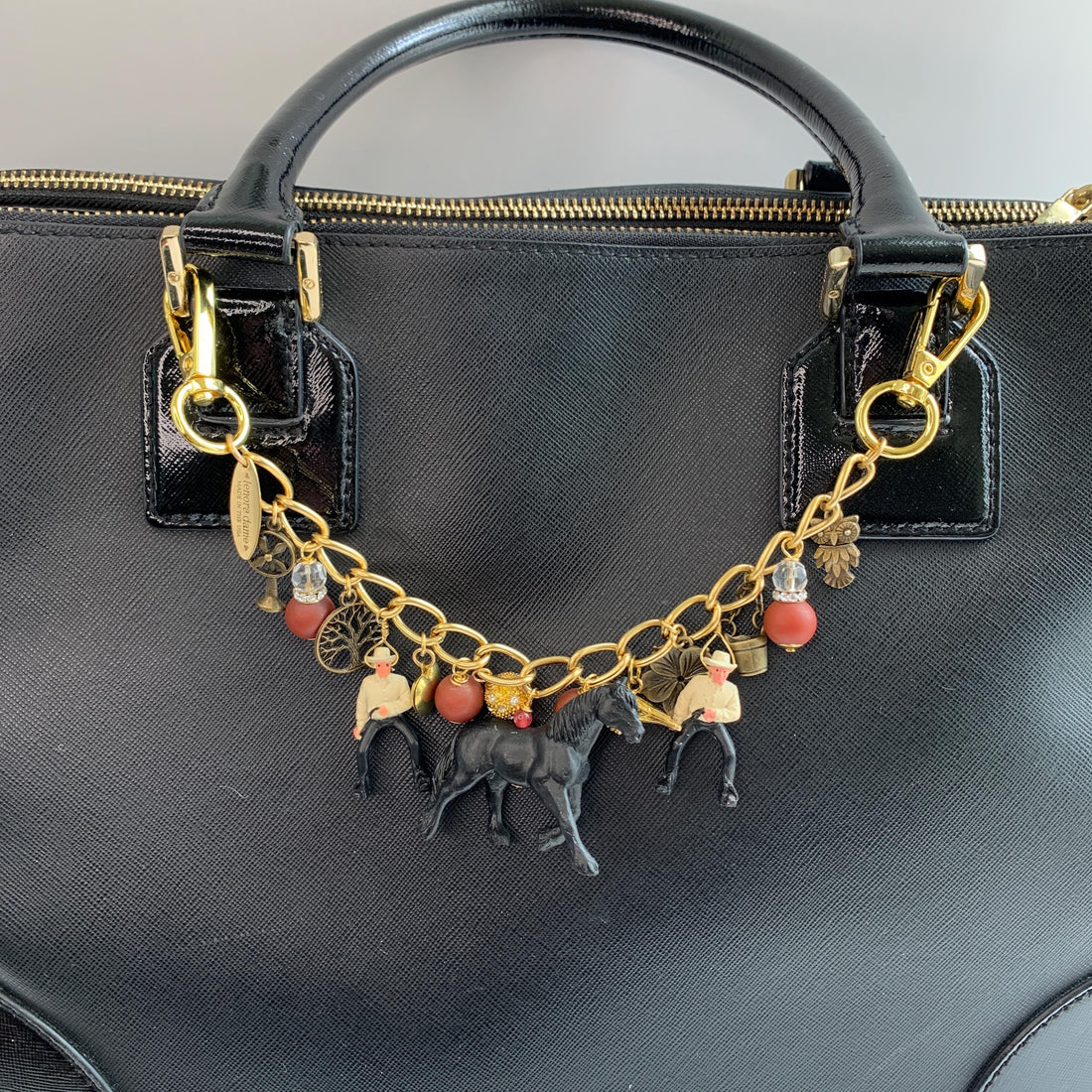 Western bag charm for handbags. Bag chain for handbag with two clasps, two cowboy charms, red beads, bronze charm including a mini bucket, owl, fan, tree and flower with a black horse figurine hanging in the middle. Lenora Dame bag charms.