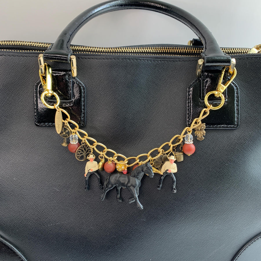 Western bag charm for handbags. Bag chain for handbag with two clasps, two cowboy charms, red beads, bronze charm including a mini bucket, owl, fan, tree and flower with a black horse figurine hanging in the middle. Lenora Dame bag charms.