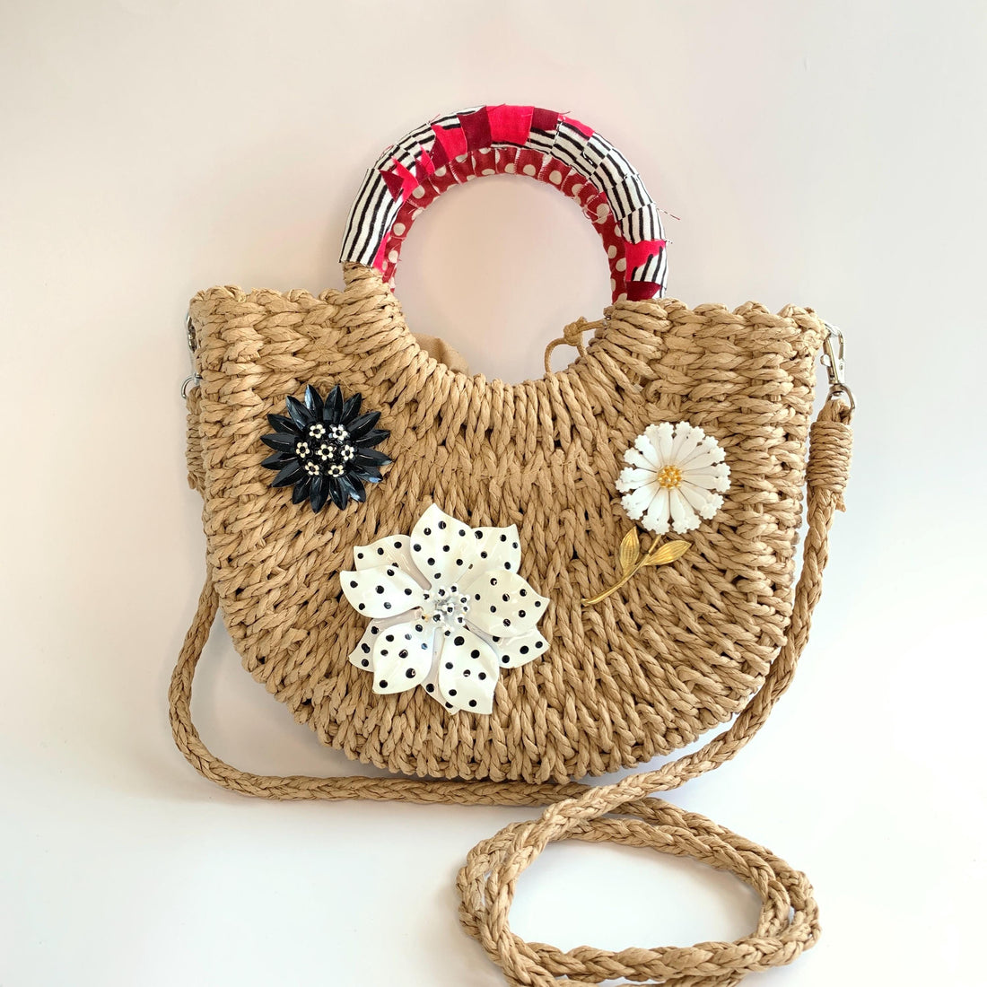 Cute straw bag for summer detailed with large metal flower brooches and contrast top handle wrapped in red and black fabric. Small woven handbag for casual summer style.