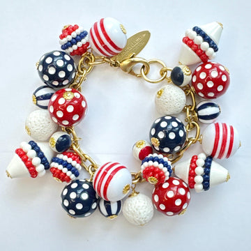 Patriotic charm bracelet with a mix of red, white and blue beads. Gold bracelet chain with lobster clasp and a Lenora Dame hang tag features blue and red round polka dot beads, and red, white and blue striped beads. Lenora Dame bracelet made in the USA.