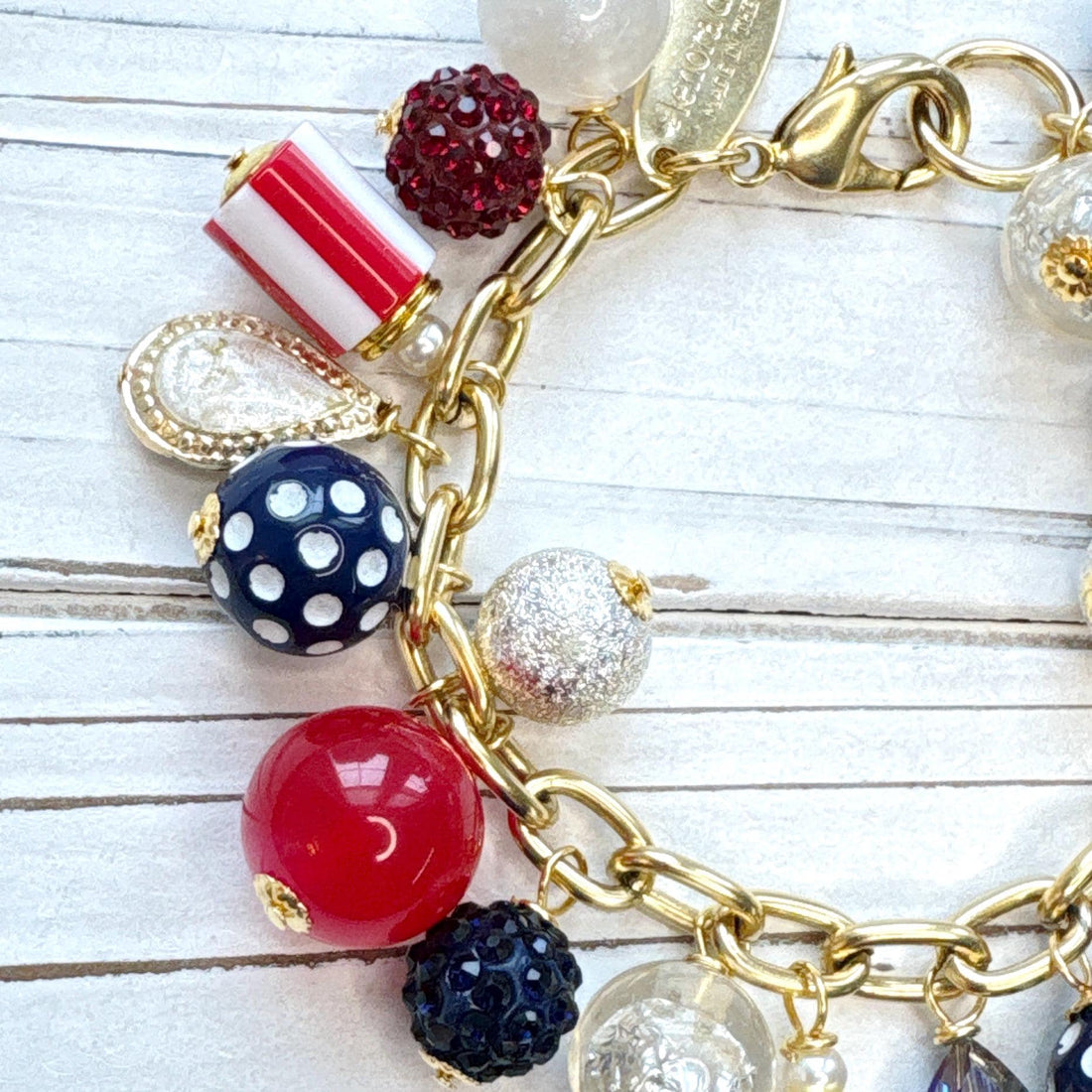 Red, white and blue charm bracelet with polka dot beads, striped beads, red rhinestone beads, and blue rhinestone beads on a gold link chain. Patriotic jewelry for women. Lenora Dame jewelry.