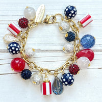 Red, white and blue charm bracelet with polka dot beads, striped beads, red rhinestone beads, and blue rhinestone beads on a gold link chain. Patriotic jewelry for women. Lenora Dame jewelry.