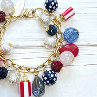 Red, white and blue charm bracelet with polka dot beads, striped beads, red rhinestone beads, and blue rhinestone beads on a gold link chain. Patriotic jewelry for women. Lenora Dame jewelry.
