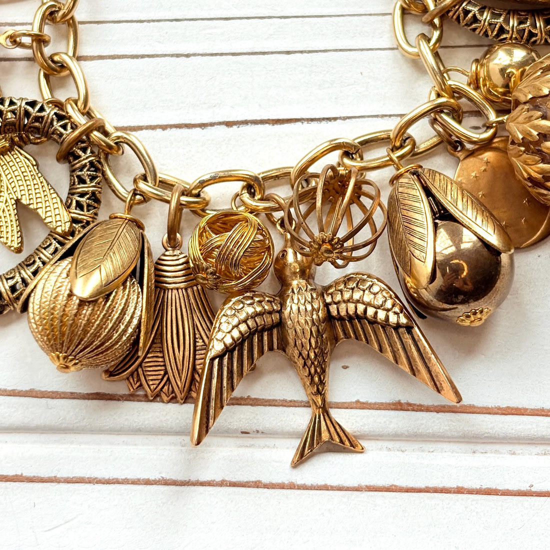 Chunky gold charm bracelet filled with a mix of gold charms in different shapes and sizes hung on a gold cable chain with lobster clasp. Lenora Dame jewelry made in the USA.