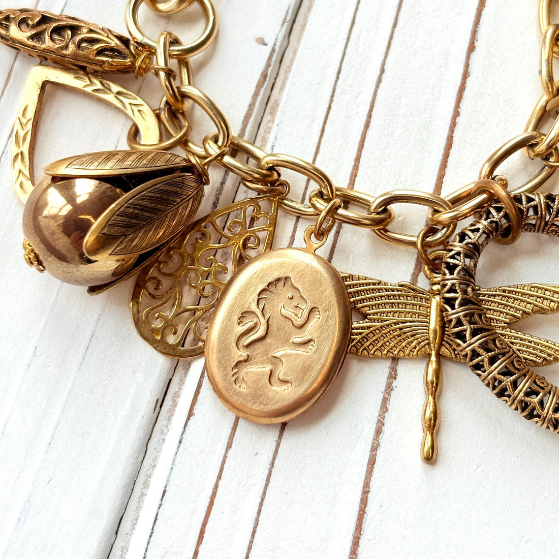 Chunky gold charm bracelet filled with a mix of gold charms in different shapes and sizes hung on a gold cable chain with lobster clasp. Lenora Dame jewelry made in the USA.