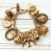 Chunky gold charm bracelet filled with a mix of gold charms in different shapes and sizes hung on a gold cable chain with lobster clasp. Lenora Dame jewelry made in the USA.