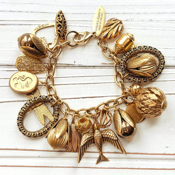 Chunky gold charm bracelet filled with a mix of gold charms in different shapes and sizes hung on a gold cable chain with lobster clasp. Lenora Dame jewelry made in the USA.