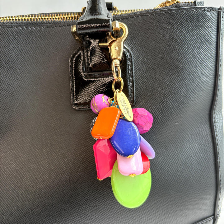 Colorful beaded bag charm with a mix of different shaped beads in a cluster under a gold trigger clasp with a gold oval charm that says Lenora Dame Made in USA. One round black and white zebra bead is among the beads. Lenora Dame bag charm.