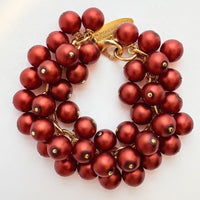 A gold chain bracelet with multiple strands of matte dark red faux pearls. The bracelet has a small tag that reads &#39;Lenora Dame&#39; and &#39;Made in the USA.&#39;