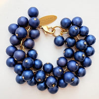 A gold chain bracelet with multiple strands of matte navy blue faux pearls. The bracelet has a small tag that reads &#39;Lenora Dame&#39; and &#39;Made in the USA.&#39;