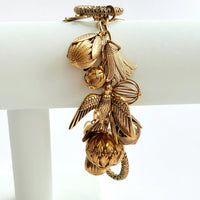 Chunky gold charm bracelet filled with a mix of gold charms in different shapes and sizes hung on a gold cable chain with lobster clasp. Lenora Dame jewelry made in the USA.