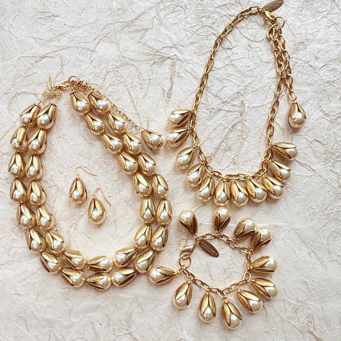 Two strand gold necklace with cream pearls encased in gold leaf bead caps, pearl and gold earrings, a gold necklace with dangling pearls with gold leaf bead caps, and a gold charm bracelet with cream pearls in gold leaf bead caps. Lenora Dame jewelry.