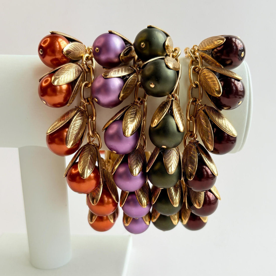 Four gold chain bracelets with pearls encased in gold leaf bead caps. Orange pearl bracelet, matte purple pearl bracelet, matte hunter green pearl bracelet and shiny dark brown pearl bracelet. Lenora Dame bracelets handmade in the USA.