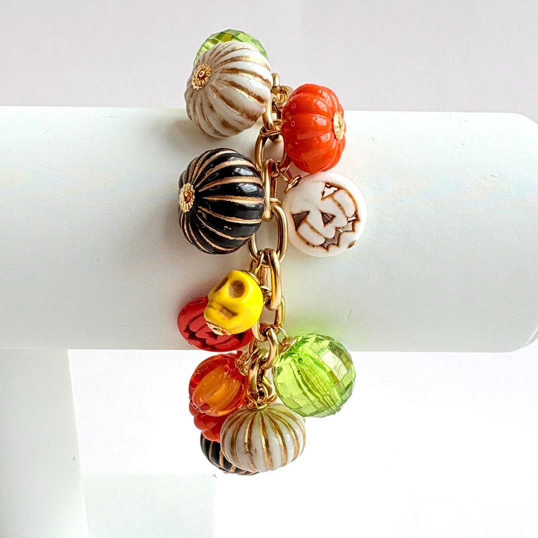 A gold chain bracelet with a variety of charms including green, orange, and white pumpkin charms, a skull charm, and a tag that reads Lenora Dame Made in the USA. Cute pumpkin charm bracelet.